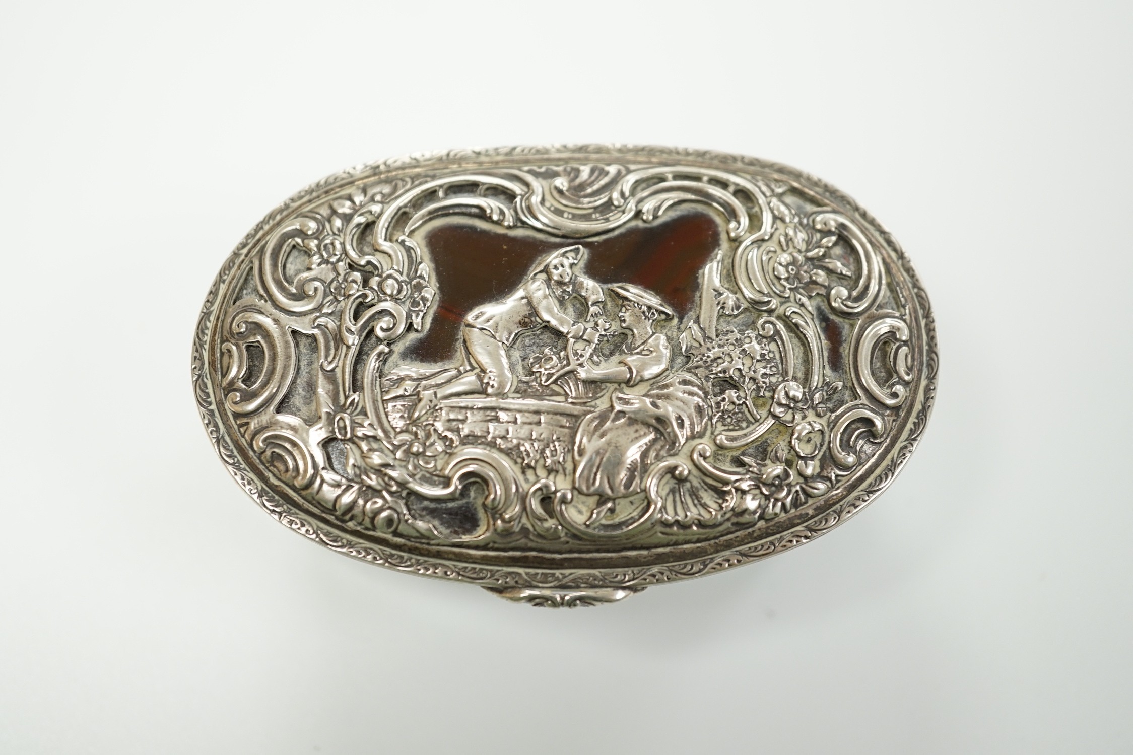 A 19th century continental white metal mounted banded agate oval snuff box, decorated with figures amid scrolls, length 79mm.
